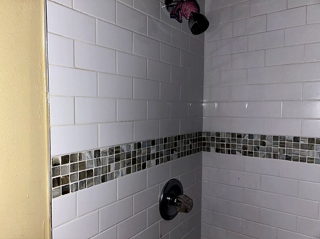 Close-up of a tiled shower wall with a glass mosaic accent band